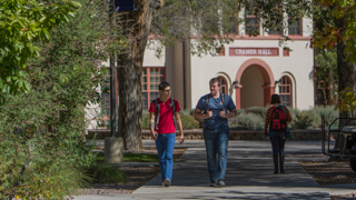 Two students are talking and walking towards the viewer, Cramer Hall can be seen in the background.